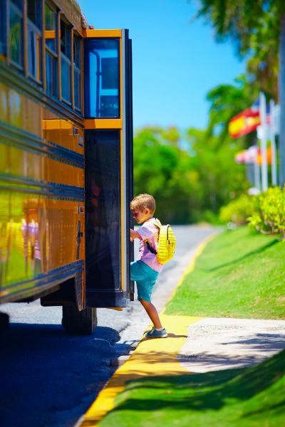 Young boy, kid getting on the school bus, ready to go to school